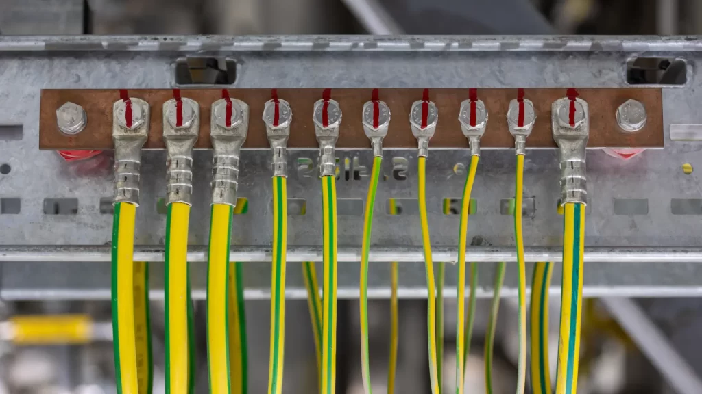 Imagem de barramento de aterramento elétrico com vários cabos verde-amarelo fixados por terminais, utilizado na proteção elétrica de instalações